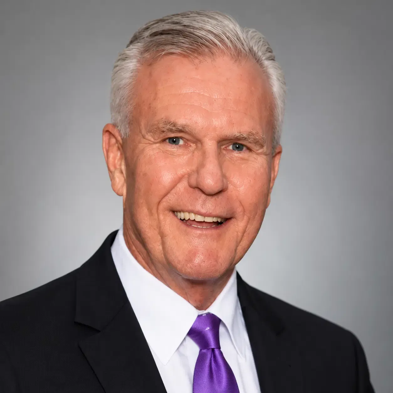 Portrait of Dr. David Tweedy, a smiling psychologist in a dark suit, white shirt, and purple tie.