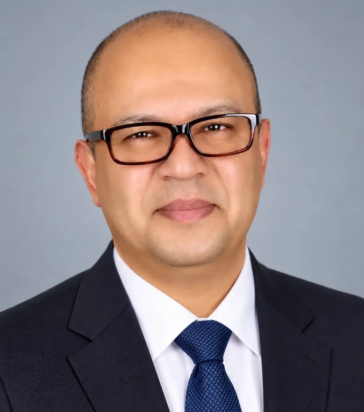 Portrait of Farooque Azam, a man wearing black glasses, a dark suit, white shirt and blue tie.