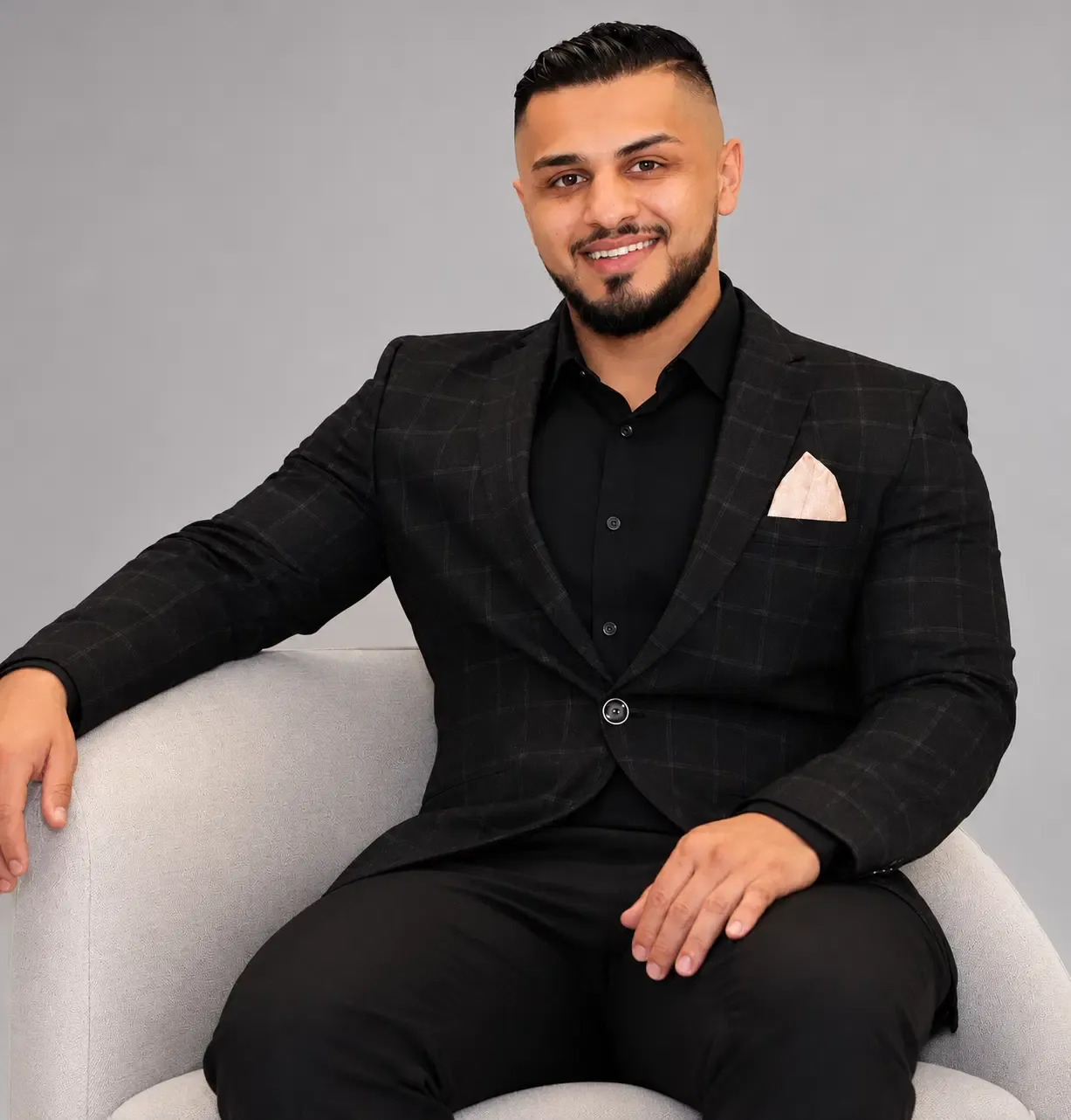 Portrait of Nazmi Hamid, a smiling man with dark hair and a beard wearing a black suit.