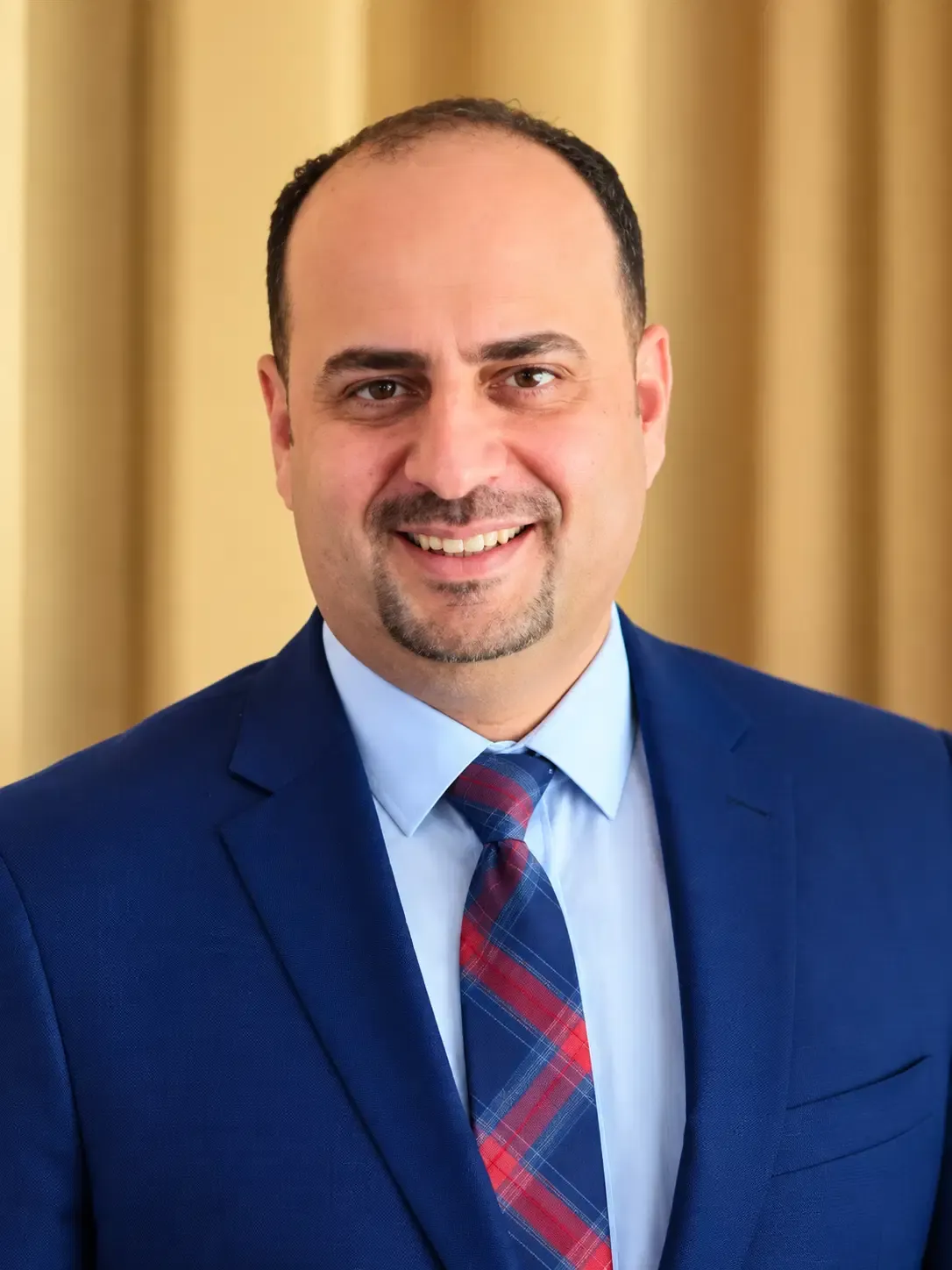 Portrait of Shadi Haddad, a smiling social worker in a navy suit and tie.
